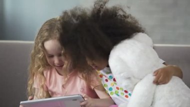 Kanepede oturan ve cep telefonu komik video izlerken çok ırklı kız teşvik