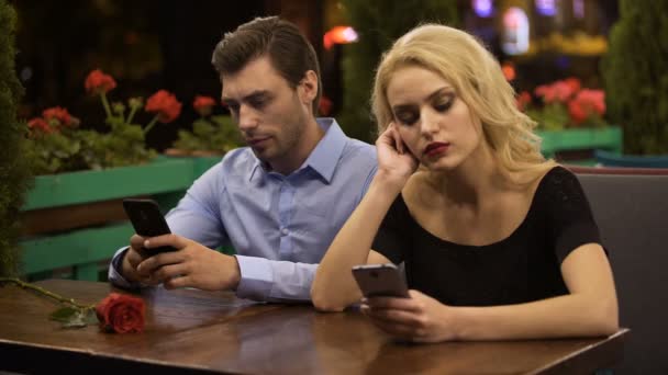 Two young people boring on date, using smartphones, problems in relationship — Stock Video