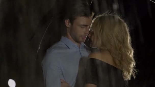 Красивая молодая пара обнимается и нежно целуется под зонтиком, под дождем — стоковое видео