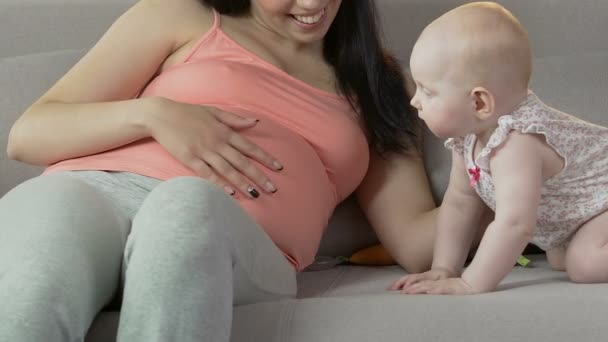 Bambino in piedi a quattro zampe sul divano, guardando la donna incinta sfregamento stomaco — Video Stock