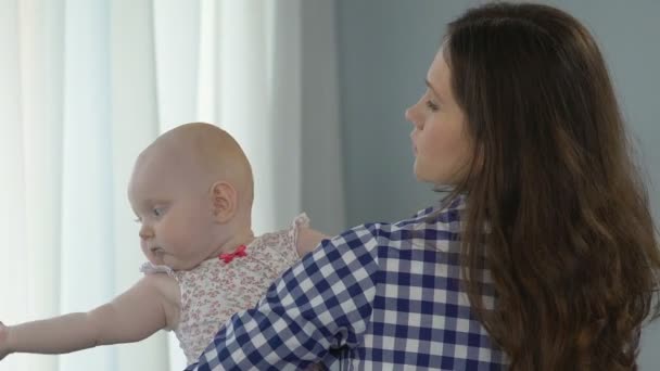 Жінка стоїть біля вікна тримає немовля, дитина дивиться плутанина обертається навколо — стокове відео