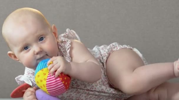 Cute baby girl lying on belly on couch, trying to bite rubber toy, nursery — Stock Video
