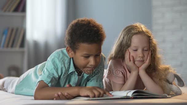 Маленькая девочка смотрит, как ее афро-американская подруга учится читать по слогам — стоковое видео