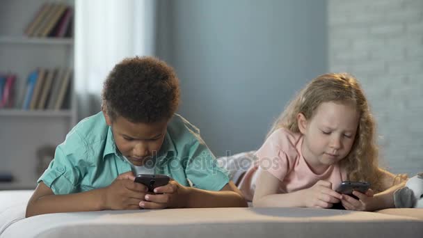 Маленькие дети, зависимые от мобильных телефонов, играют в игры с концентрированными лицами — стоковое видео