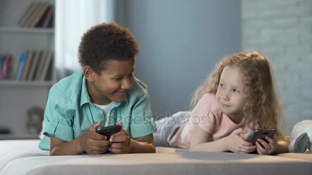 Sonrientes niños jugando juegos en línea en la aplicación móvil, adicción a los gadgets — Vídeo de stock