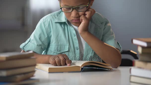 Niño inteligente en gafas sentado en la biblioteca leyendo libros, literatura educativa — Vídeos de Stock