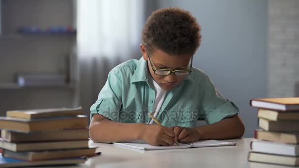 Slimme kleine jongen netjes schrijven huiswerk in zijn notitieblok, ijverig schooljongen — Stockvideo