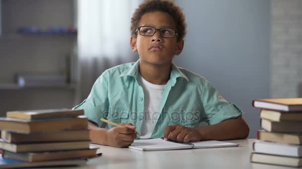 Афро-американский мальчик думает о школьном эссе, умный ребенок делает домашнее задание, образование — стоковое видео