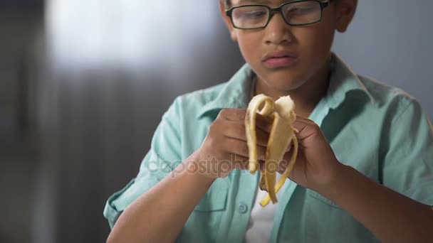 Niño afroamericano comiendo plátano sabroso durante el descanso en la escuela, bocadillo saludable — Vídeo de stock
