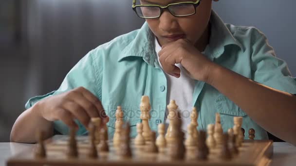 Младший ученик принимает участие в шахматных соревнованиях, обдумывая стратегию, хобби — стоковое видео