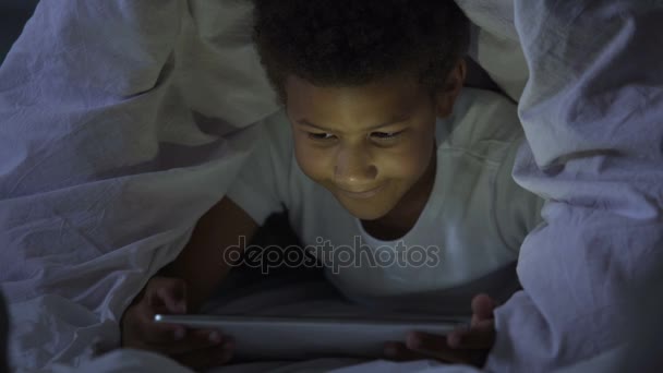 Pequeño niño mirando la tableta en secreto por la noche, cubierto con la cabeza en manta — Vídeos de Stock