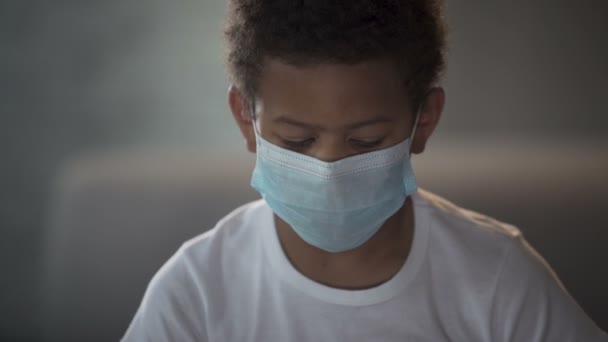 Афроамериканский ребенок в медицинской маске смотрит в камеру с грустными глазами — стоковое видео