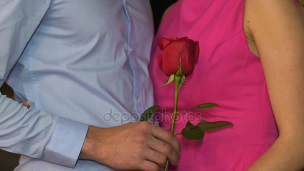 Hombre y mujer de pie cerca el uno del otro, hombre sosteniendo rosa roja, citas, amor — Vídeos de Stock
