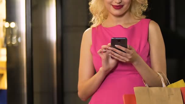 Chica con bolsas de compras celebración de teléfono celular y pantalla de desplazamiento, descuentos en línea — Vídeo de stock
