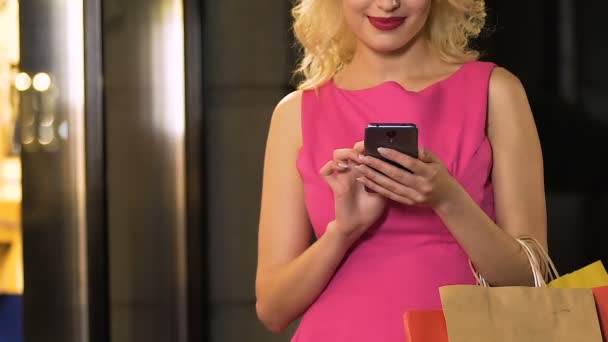 Girl with shopping bags holding cellphone and scrolling screen, online discounts — Stock Video