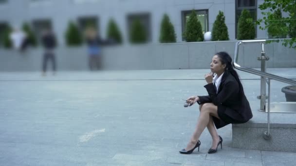Mujer en traje de negocios sentada cerca del centro de negocios, pensando, hora del almuerzo — Vídeo de stock