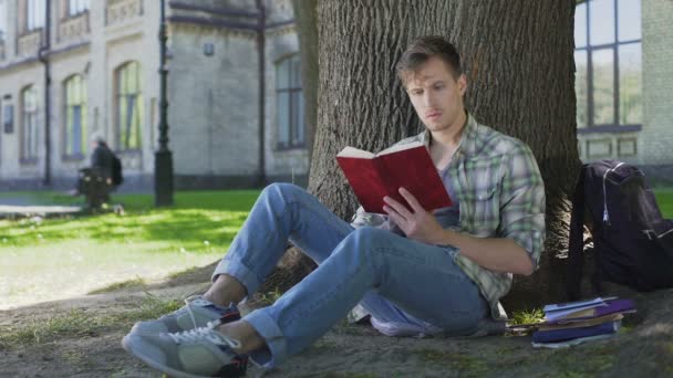 Junger Mann liest Buch mit faszinierender Handlung, einfühlsam mit Charakteren — Stockvideo