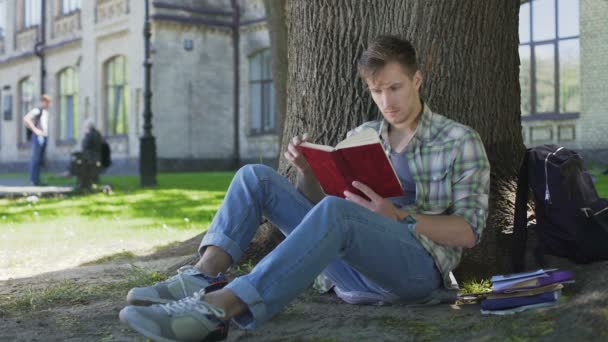 Студент-мужчина просматривает страницы учебника, повторяет выученный материал — стоковое видео