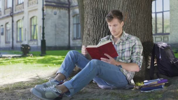 Guy termine la lecture du chapitre du livre, pensant à l'histoire assis à l'ombre de l'arbre — Video