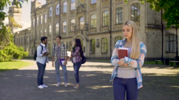 Samotna dziewczyna stojąc z dala od przyjaciół, zdenerwowany o plotki na Uniwersytecie — Wideo stockowe