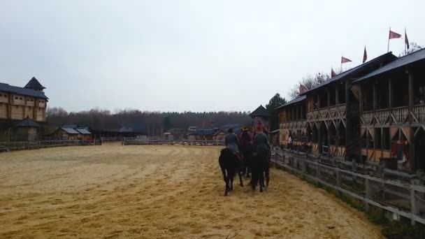 Maschi equitazione cavalli giù arena sabbiosa lungo costruzioni fortificanti in legno, fest — Video Stock