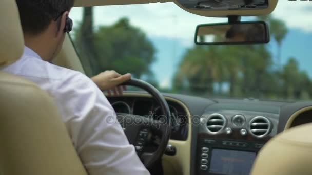 Masculino condução de carro de luxo, tendo conversa sobre fone de ouvido, ocupado homem de negócios — Vídeo de Stock