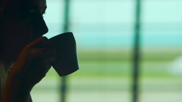 Silhouet van de vrouw koffie drinken in café tegen grote raam, wachten luchthaven — Stockvideo