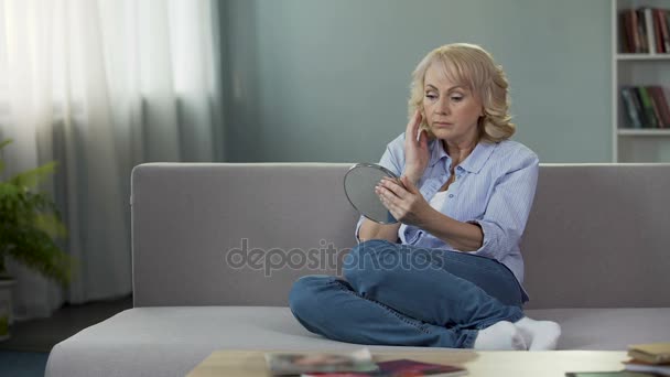 Middle-aged lady sitting at home and looking into a hand mirror, retirement — Stock Video