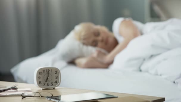 In mattinata. Donna di mezza età che dorme a letto. Vista del tavolo con orologio — Video Stock