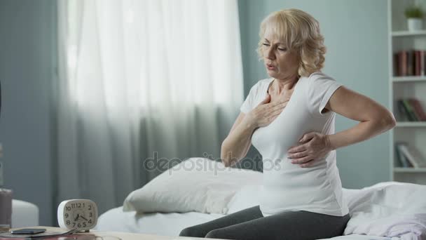 Pretty mature woman sitting on bed and suffering from heart attack, health — Stock Video