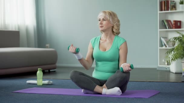 Attraktive Seniorin sitzt auf dem Boden und hebt Hanteln, trainiert — Stockvideo