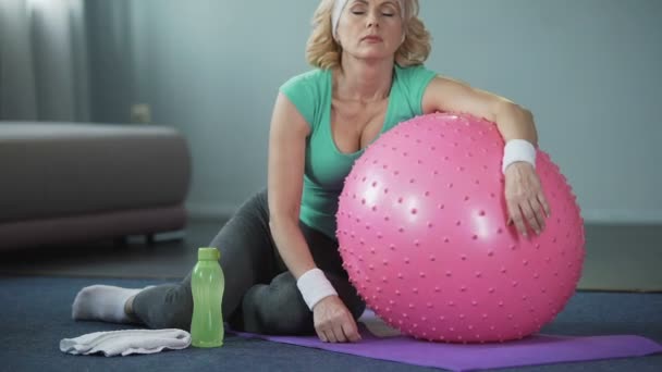 Виснажена зріла жінка лежить на фітнес-кулі, розслабляючись після активного тренування — стокове відео