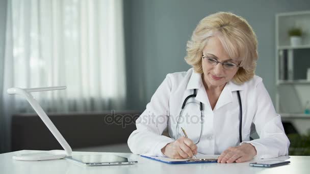 Женщина-врач выписывает рецепты, заполняя медицинские карты пациентов — стоковое видео