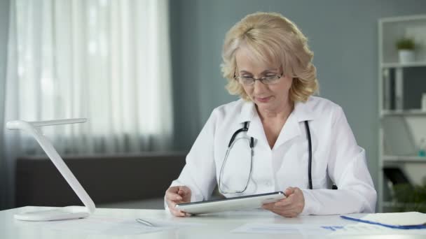 Médico especialista revisando pacientes resultados de testes em tablet sentado no armário aconchegante — Vídeo de Stock