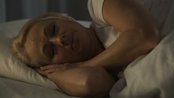 Жінка середнього віку посміхається, спить зі звуковим сном, відчуває спокій і блаженство — стокове відео
