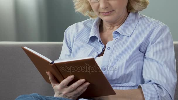 Mujer jubilada sentada en el sofá y leyendo libro, ávido lector de libros, tiempo libre — Vídeos de Stock