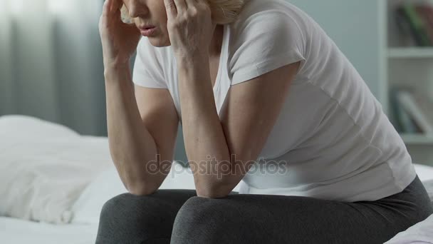 Femme retraitée assise sur le bord du lit, se frottant les tempes, problèmes de santé, point culminant — Video