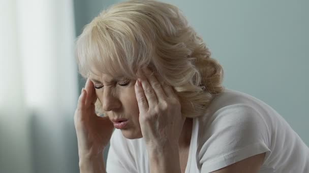 Mujer anciana frotando las sienes intensamente, dividiendo el dolor de cabeza, problemas de salud — Vídeos de Stock