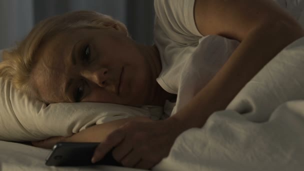 Ensam mogen kvinna ligger i sängen och tittar på familj foto på mobiltelefon, sömnlöshet — Stockvideo