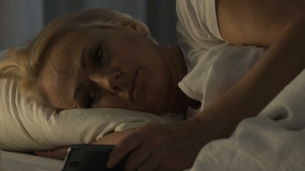 Triste pensionista mujer charlando en el teléfono inteligente y tratando de dormir, insomnio — Vídeos de Stock