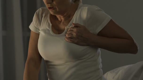 Pensionerad kvinna som sitter på soffan och lider av hjärtattack, hälsoproblem — Stockvideo