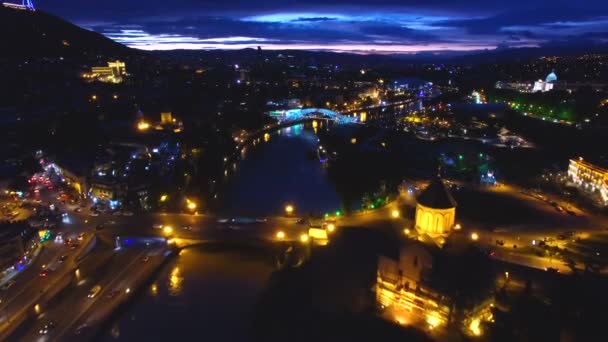 Krásná řeka proudí pod osvětlené město mosty po setmění, letecký snímek — Stock video