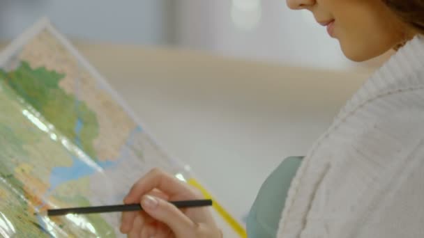 Молодая женщина держит карандаш над картой, планируя маршрут путешествия, отдыхая — стоковое видео