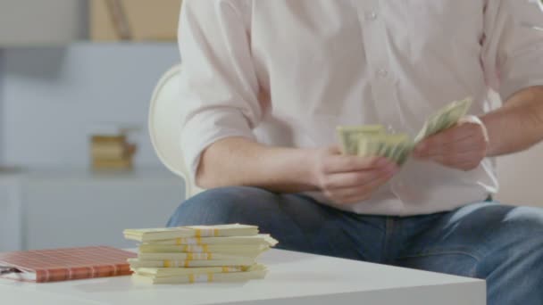 Hombre rico contando dólares en las manos, poniéndolos en la mesa junto a los fajos, la riqueza — Vídeos de Stock