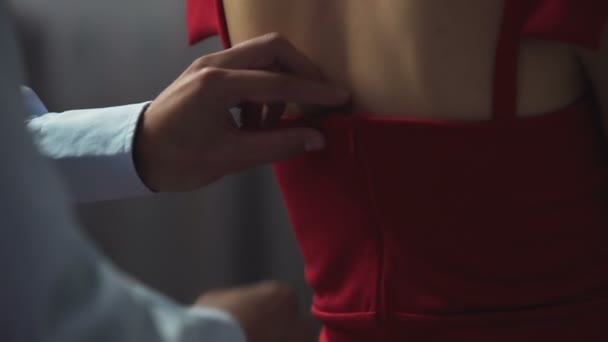Мужчина медленно расстегивает красное платье сзади, обнажая обнаженную женскую спину — стоковое видео