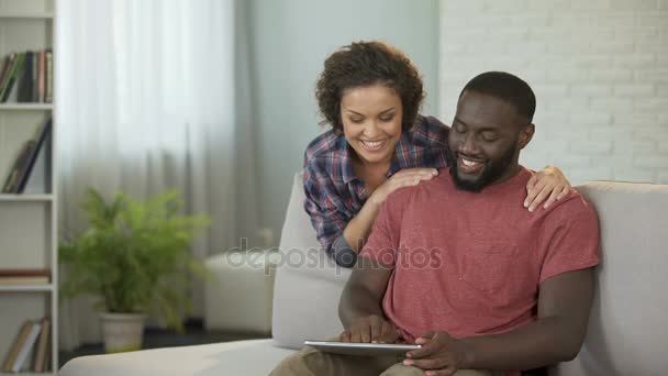 Щасливий чоловік консультує з дружиною про покупку нової машини, показуючи пропозиції на планшеті — стокове відео