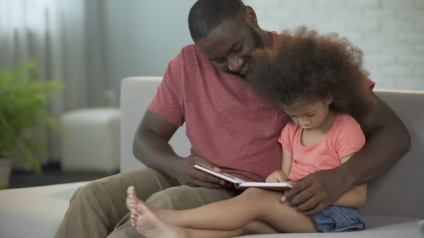 Liebevoller Vater sieht zu, wie seine kleine gelockte Tochter lesen lernt — Stockvideo