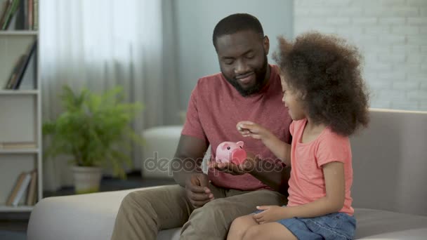 Заботливый отец учит ребенка экономить деньги, класть монеты в копилку — стоковое видео