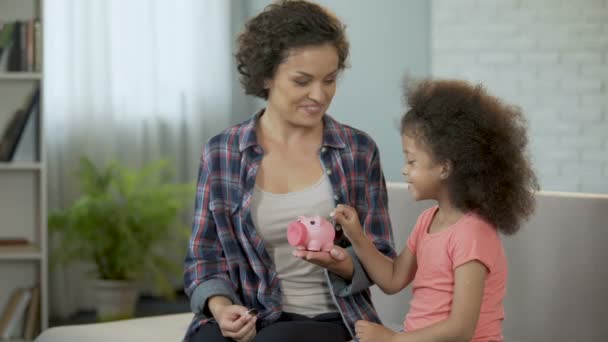 Mamá y su hija lanzando monedas en alcancía, ahorrando dinero para regalos — Vídeo de stock