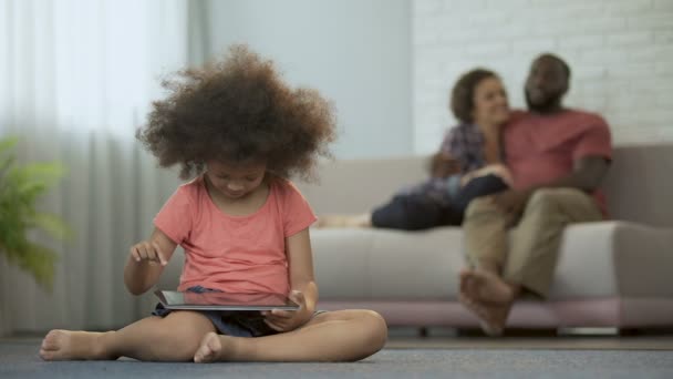 Молоді батьки насолоджуються спільним проведенням часу, спостерігаючи, як їх дочка грає на планшеті — стокове відео